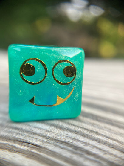 Tusktooth Fjord Inspired D6 – Handmade Glow-in-the-Dark Green & Blue Gaming Die with Gold Grinning Face